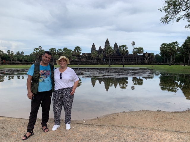 Two people posing with Angkor Wat in the background by a pond.