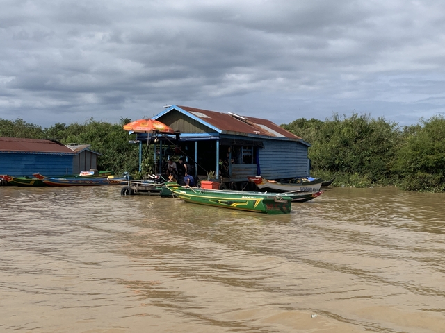       Floating houses and boats on a river under a cloudy sky.
  