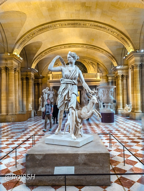 Statues in a grand indoor gallery filled with visitors.
