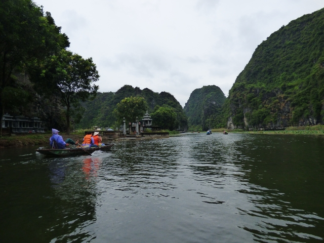       People rowing boats on a river surrounded by lush hills.
  