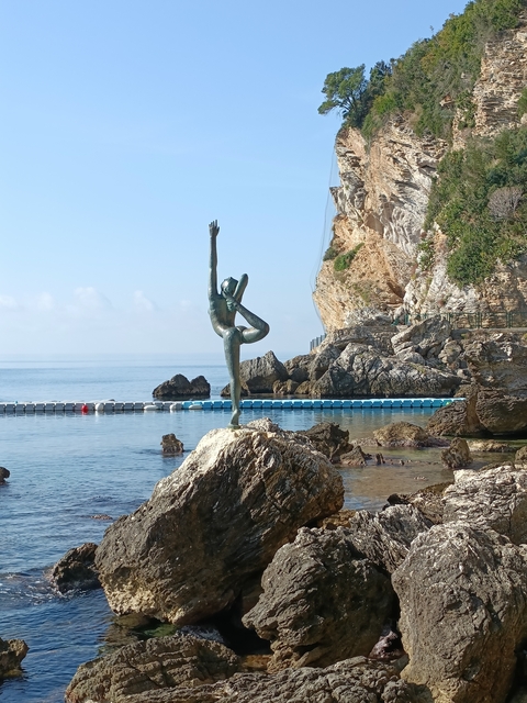 Statue on a rock beside the sea with clear sky.