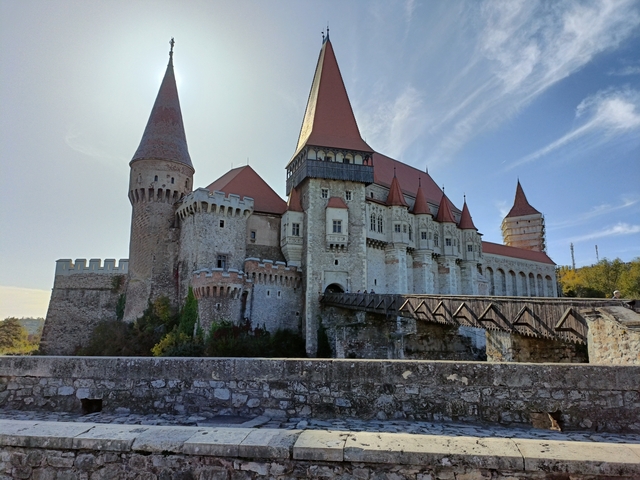 Panoramic view of a castle with red roofs under a blue sky.