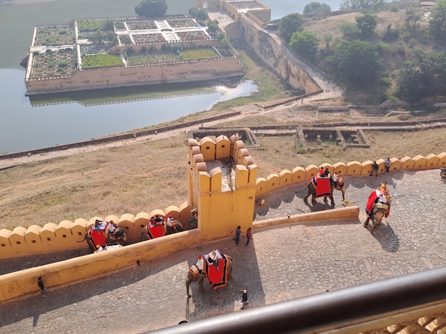 Tourists riding elephants on a fort's walls with a scenic view.