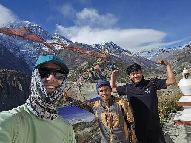 A group of hikers posing in front of mountainous scenery with prayer flags.