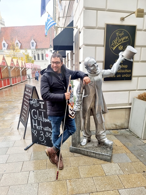 A man posing with a statue on a shopping street.