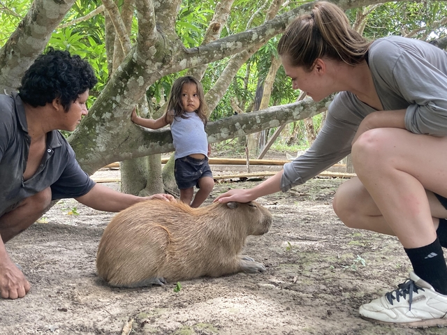       Family petting a capybara under a tree.
  