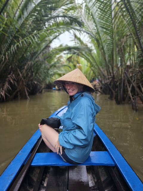 Woman enjoying a boat ride with conical hat in a waterway.