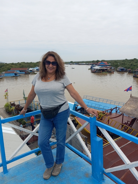 Woman standing on a lookout with floating village and Cambodia flag visible.