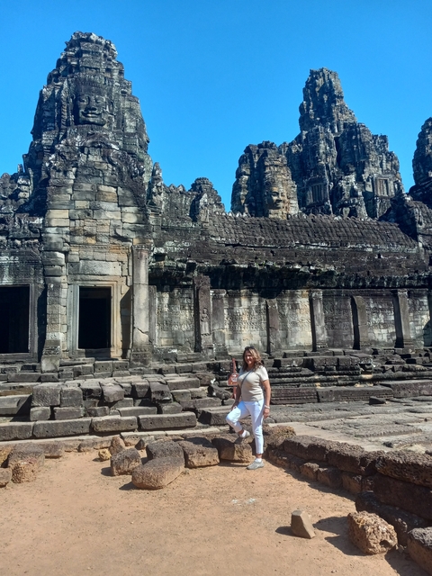 Woman standing near Bayon Temple in Angkor Thom with stone faces.