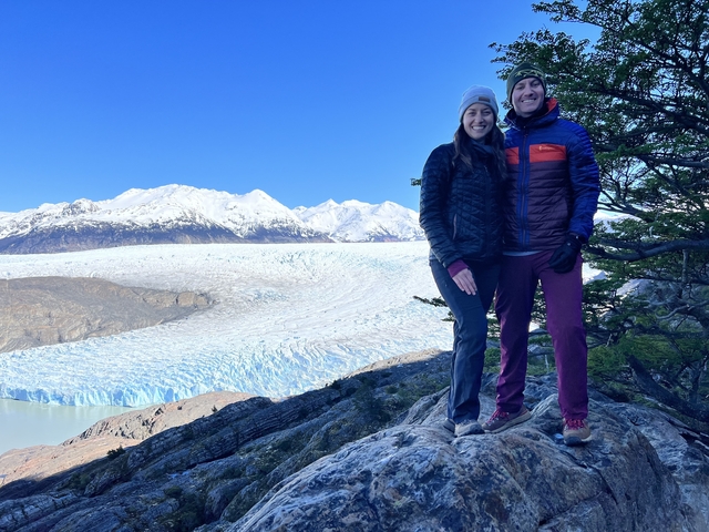 Couple standing in front of a vast glacier with snowy mountains.