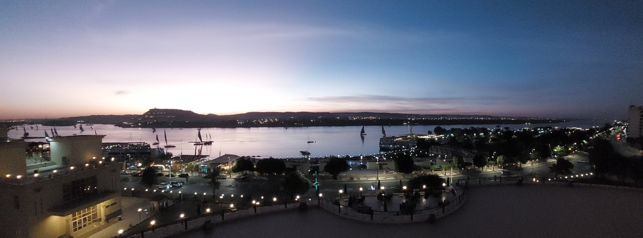 Cityscape view at dusk with a river and boats.