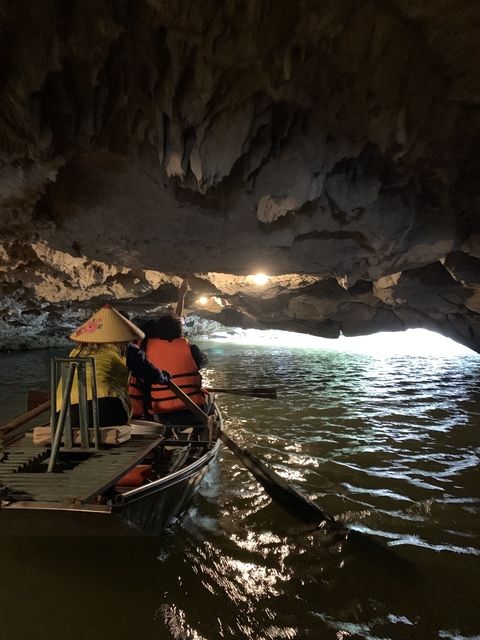       Two people in traditional attire rowing a boat inside a cave.
  