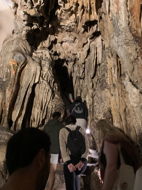 People exploring a dark cave with stalactites.