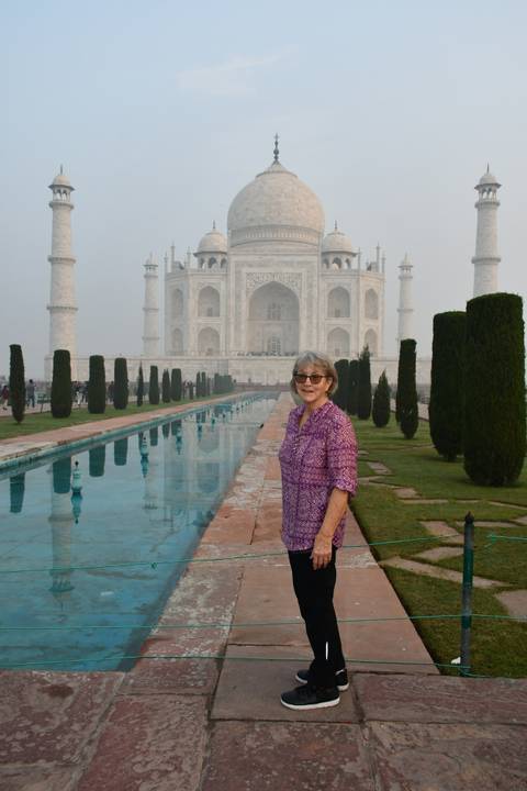 Woman standing in front of the Taj Mahal with reflecting pool.