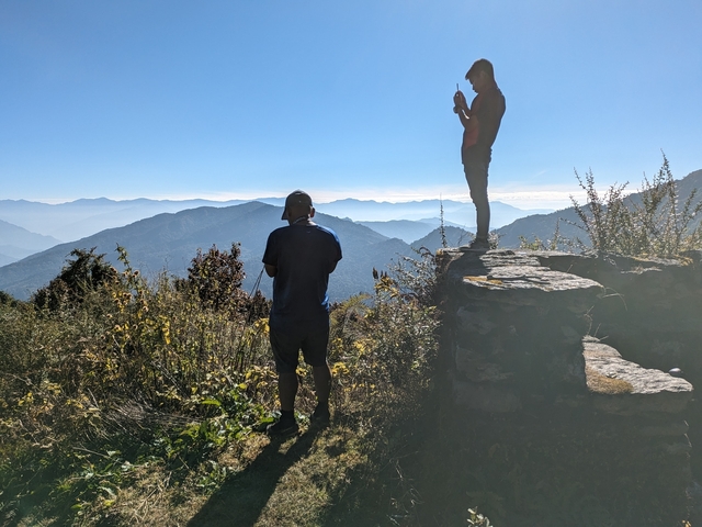       Two people standing with a scenic mountainous landscape.
  