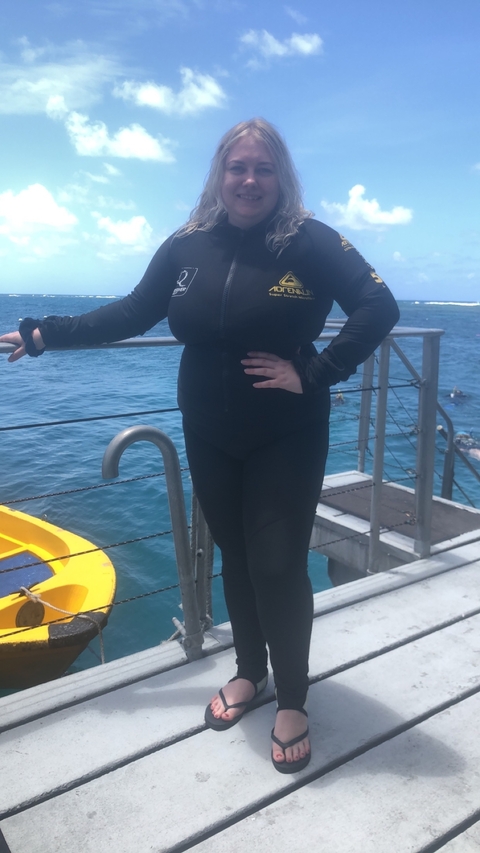       Person in a wetsuit standing on a boat near the ocean.
  