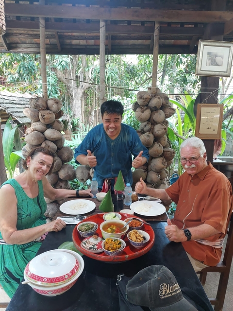       Three people smiling at a dining table with Thai cuisine.
  