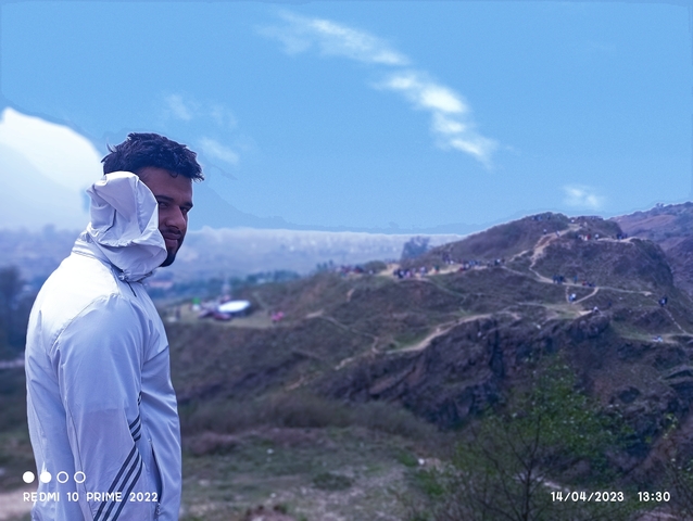      Person in a white jacket against a scenic mountainous backdrop.
  