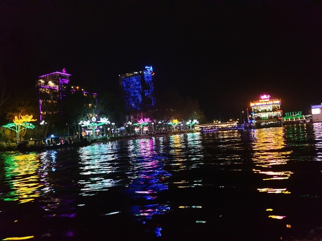 Vibrant night scene of a bustling riverside area with colorful lights.