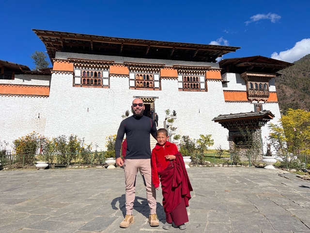       Man and young monk in front of a Bhutanese building.
  