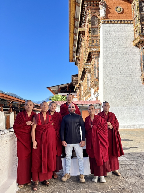       Person posing with monks in front of a traditional Bhutanese building.
  
