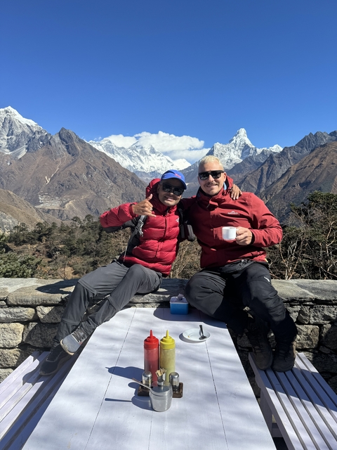       Two men sitting with mountains in the background.
  