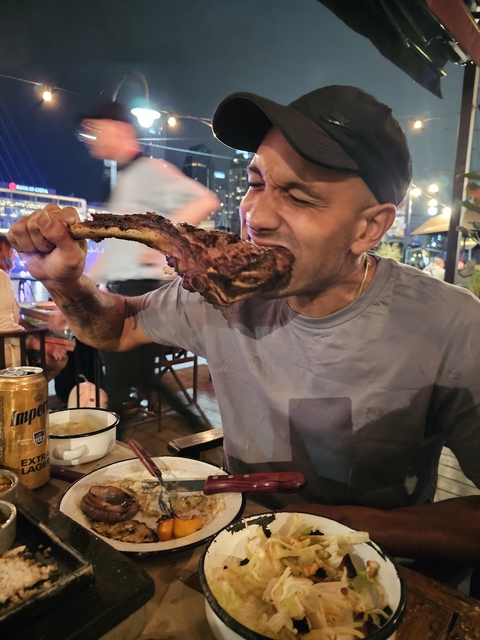 Person enjoying a large piece of grilled meat at a restaurant.
