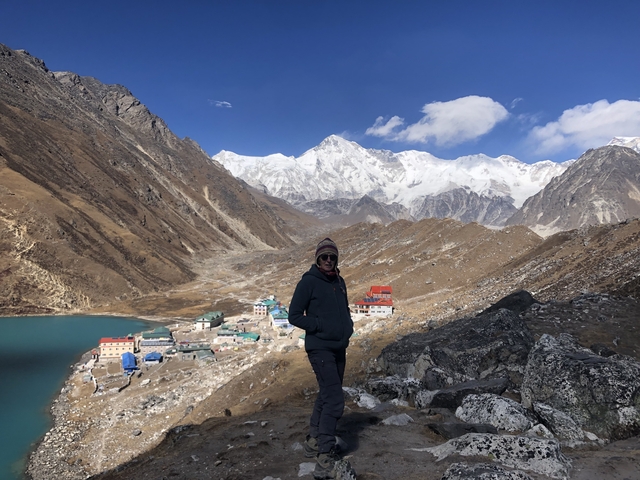       A person posing in front of a mountainous landscape with a lake.
  