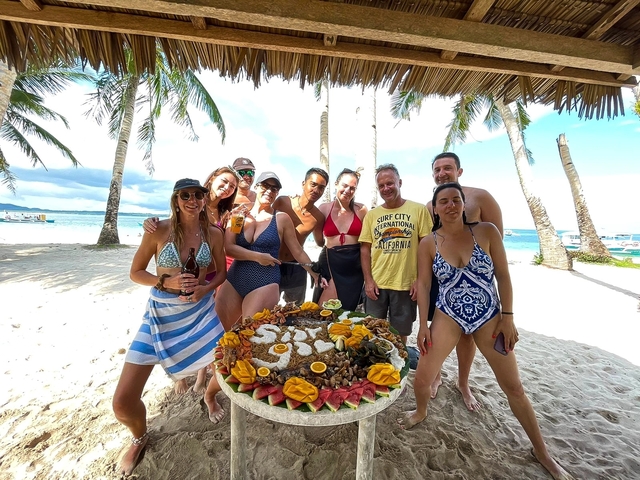 Group of people posing with a food display on a beach.
