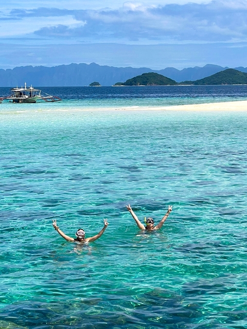 People swimming in clear blue water near a beach.