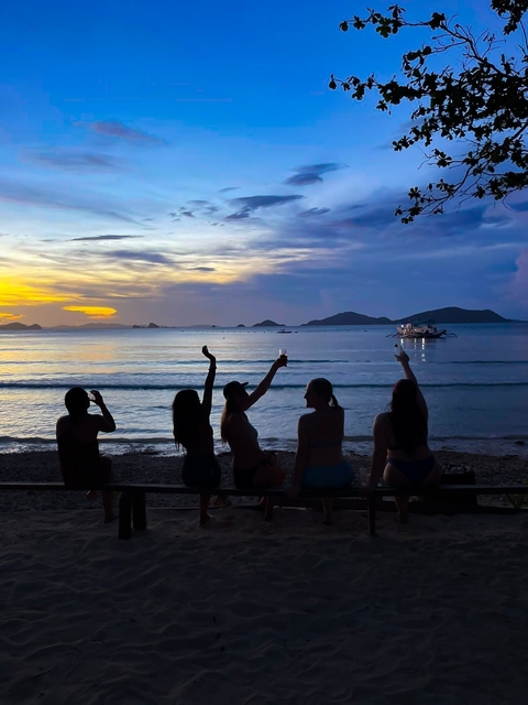       Silhouettes of people sitting on a beach at sunset.
  
