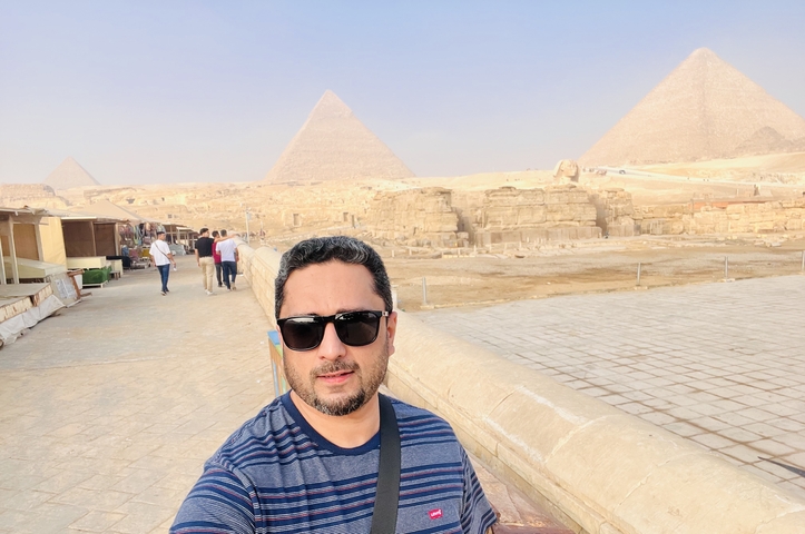 Person taking a selfie with pyramids in the background.