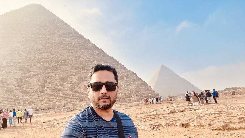 Person posing with pyramids in the background.