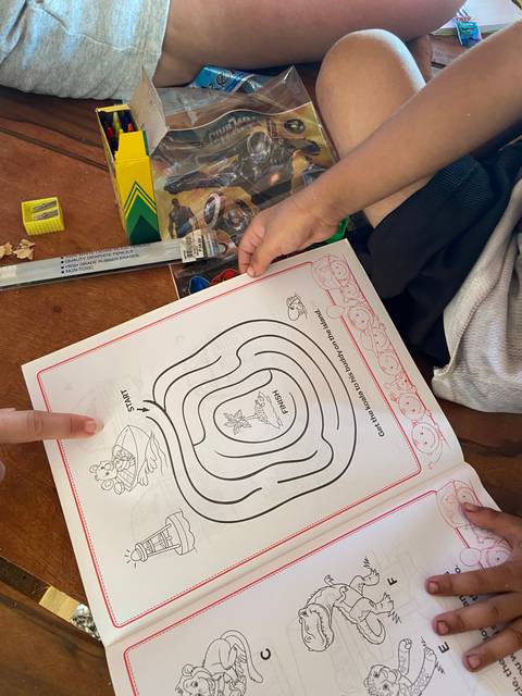       Child drawing in a coloring book on a wooden table with crayons.
  