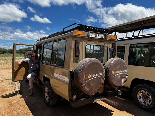 Person leaning against a safari vehicle with others around.