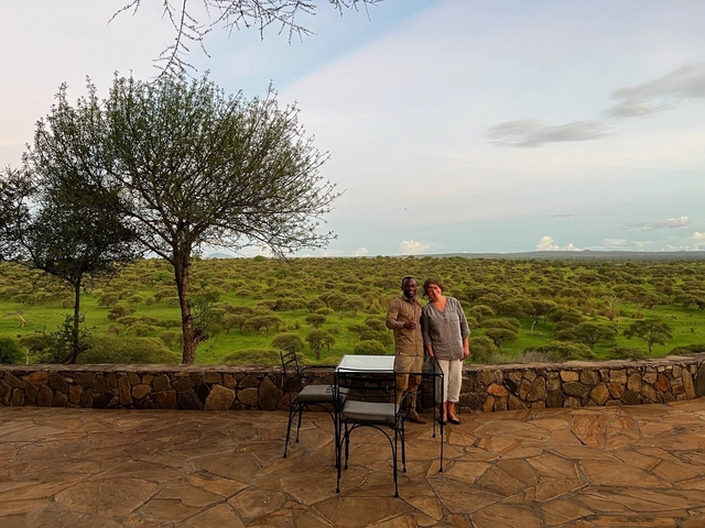       Couple posing on a terrace with a scenic view of trees and plains.
  