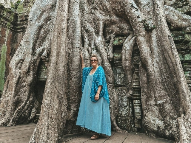 Person standing beside massive tree roots at a temple.