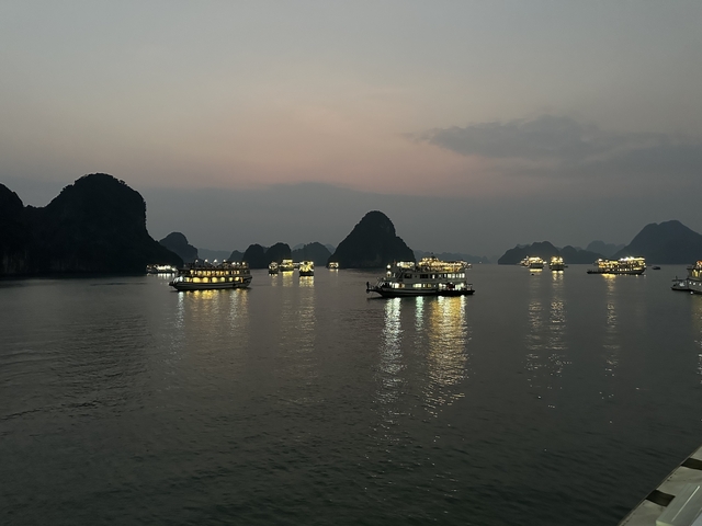       Boats with lights on a tranquil bay during twilight, likely in Halong Bay, Vietnam.
  