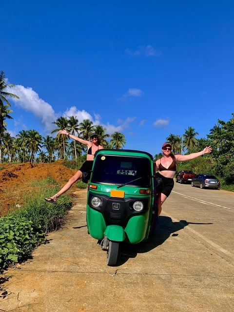 Two people posing with a green tuk-tuk surrounded by palm trees in the Philippines.