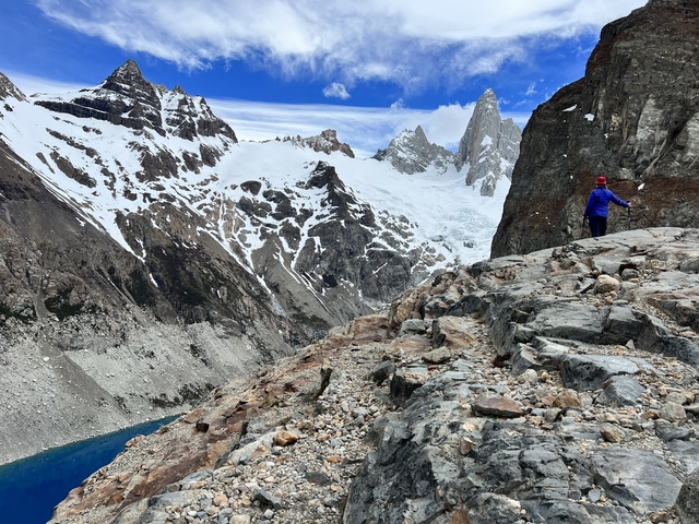 A person on rocky terrain with a view of snowy mountains and blue sky.