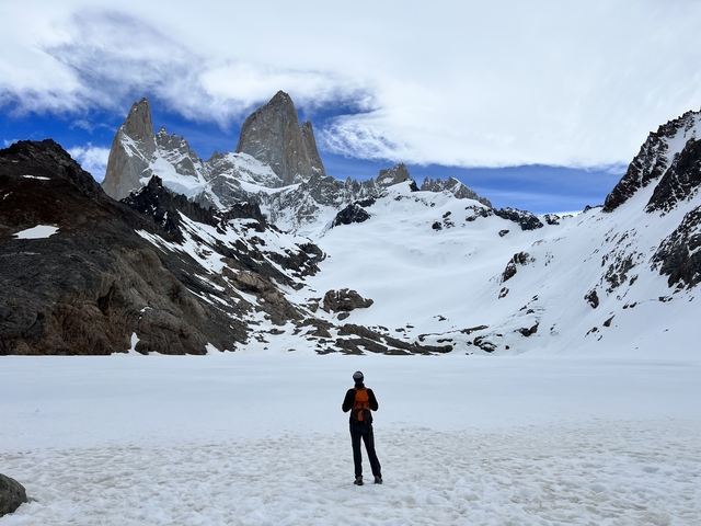 A person standing on snow in front of towering mountains in a national park.