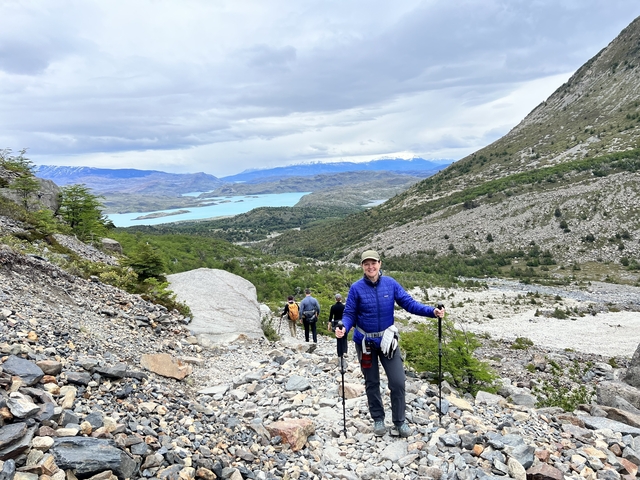 People hiking on a rocky path with a vast landscape and a lake in the distance.