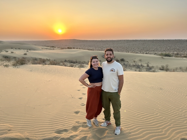 A couple standing on sand dunes at sunset, likely in Jaisalmer, India.