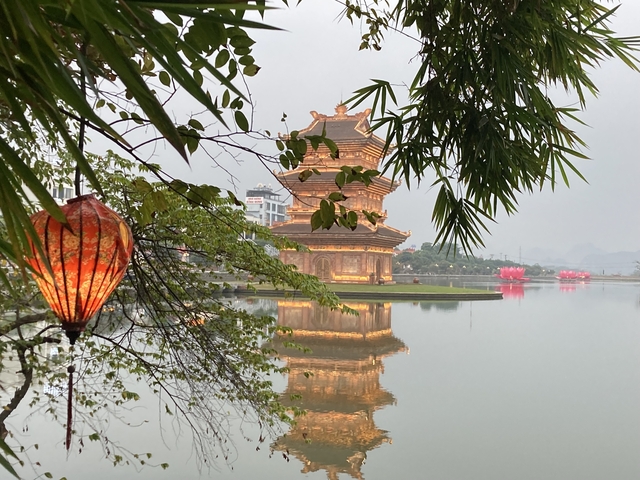       A pagoda reflected in water with lanterns hanging from trees.
  