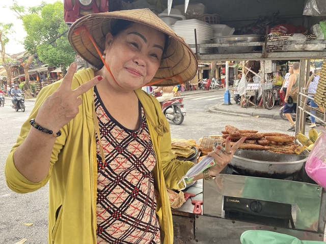       A woman with food in front of a street food cart.
  