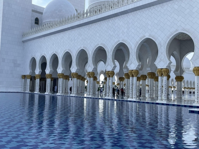 Tourists at a mosque with arches and water in front.
