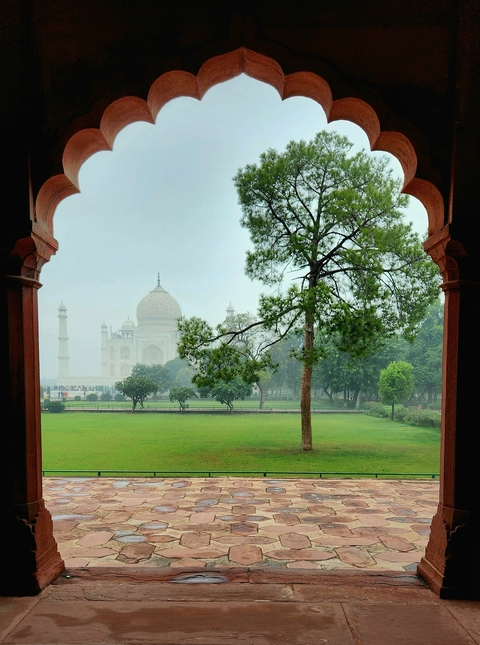 Taj Mahal viewed through a beautifully arched window with green gardens.