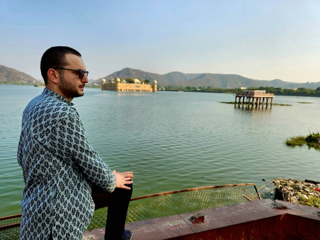 Person looking out over a scenic lake with mountains in the background.