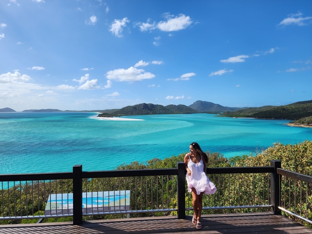 Woman standing on a balcony overlooking turquoise waters and islands.