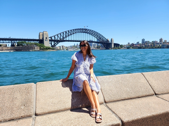       Woman sitting by the water with a city skyline and a famous bridge in the background.
  